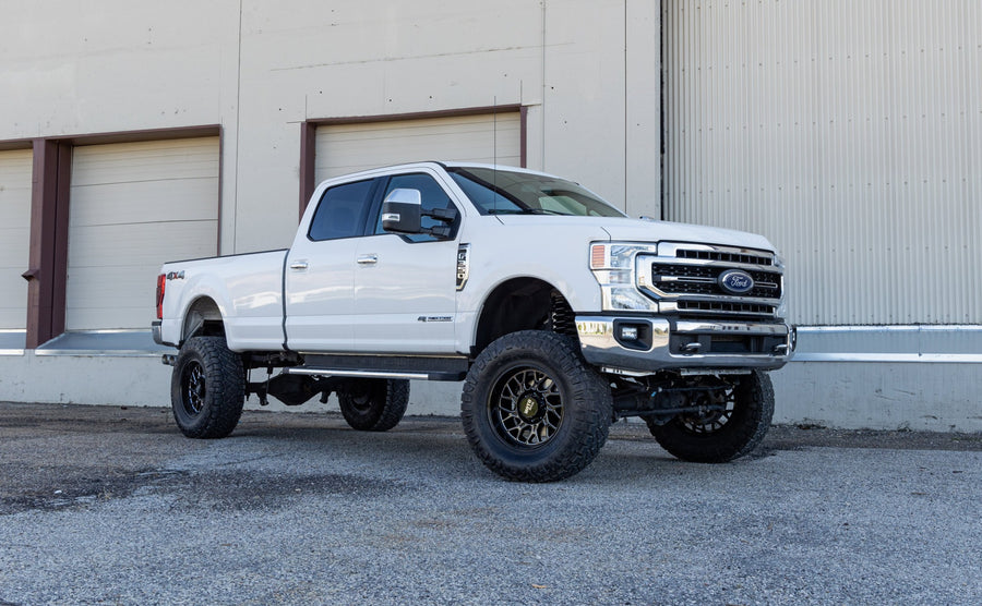 ReadyLIFT Lift Kit installed on a Ford F-250 Super Duty: white Ford Super Duty crew cab long bed lifted on bronze wheels in front of a warehouse