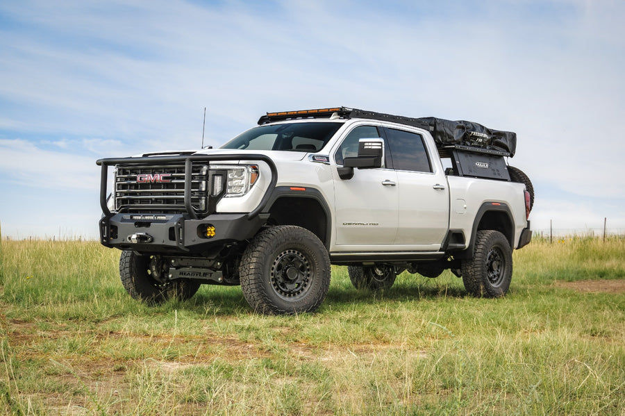 ReadyLIFT Lift Kit installed on a GMC Sierra 2500HD: white GMC Sierra HD crew cab lifted with an aftermarket bumper, roof rack and bed tent in a grassy field