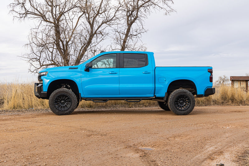 ReadyLIFT MAX3.3 Suspension System installed on a Chevrolet Silverado 1500: bright blue Chevrolet Silverado 1500 crew cab lifted, side profile on a dirt road