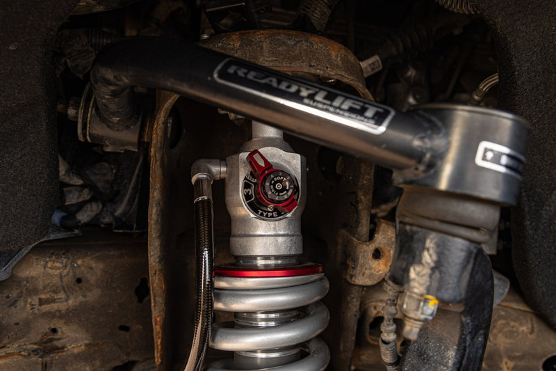 ReadyLIFT MAX3.3 Suspension System on a vehicle: ReadyLIFT upper control arm over a Falcon coilover with red adjuster installed in a wheel well