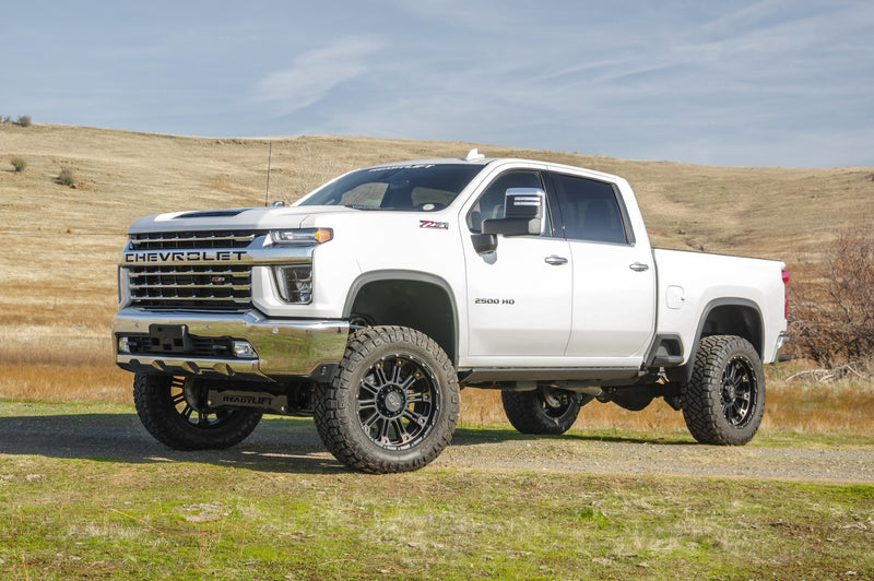 ReadyLIFT MAX3.3 Suspension System installed on a Chevrolet Silverado 2500HD: white Chevrolet Silverado 2500HD crew cab lifted on black wheels in a grassy field, front quarter view
