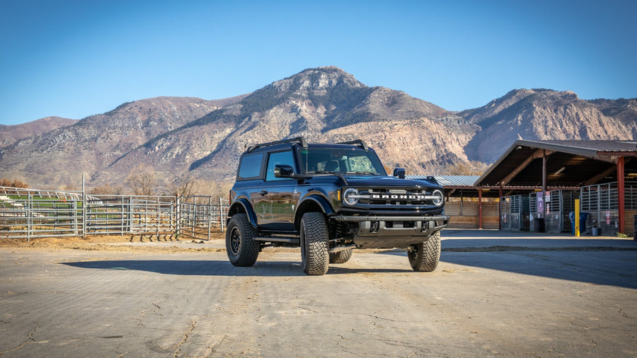 ReadyLIFT SST Lift Kit installed on a Ford Bronco: A black lifted Ford Bronco two-door parked on a ranch lot with mountains behind