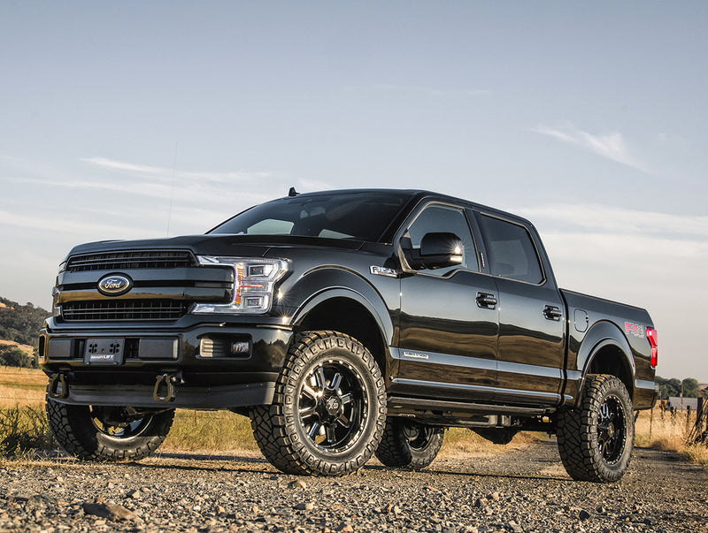 ReadyLIFT SST Lift Kit installed on a Ford F-150: A black lifted Ford F-150 SuperCrew on off-road tires parked on gravel