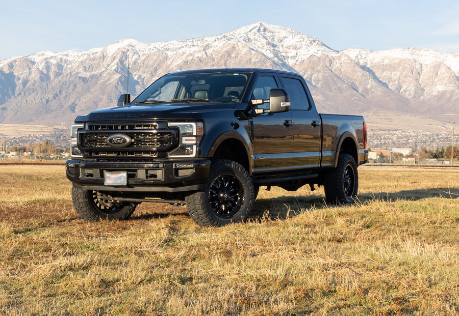 ReadyLIFT SST Lift Kit installed on a Ford F-250 Super Duty: A black lifted Ford Super Duty Crew Cab parked in a field with snowy mountains behind