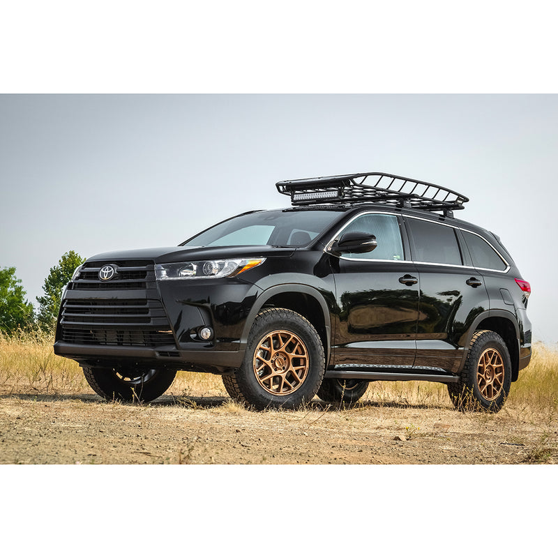 ReadyLIFT SST Lift Kit installed on a Toyota Highlander: A black lifted Toyota Highlander with a roof basket and bronze wheels parked in a dry field