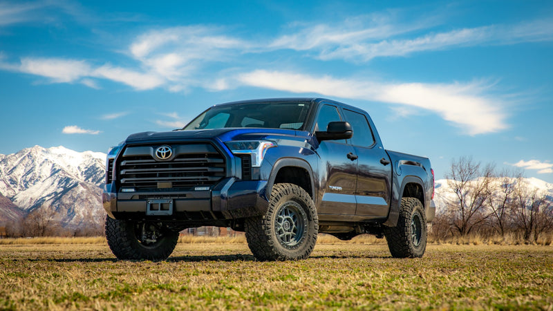 ReadyLIFT SST Lift Kit installed on a Toyota Tundra: A dark blue lifted Toyota Tundra CrewMax parked on grass with snowy mountains behind