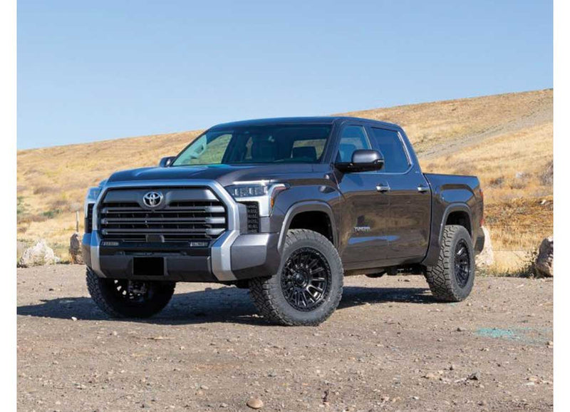 ReadyLIFT SST Lift Kit installed on a Toyota Tundra: A dark gray lifted Toyota Tundra CrewMax parked on a gravel lot with dry hills behind