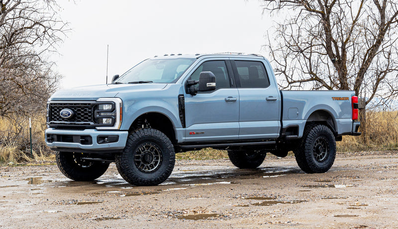 ReadyLIFT SST Lift Kit installed on a Ford F-250 Super Duty: A light blue lifted Ford Super Duty Tremor Crew Cab parked on a muddy lot with bare trees