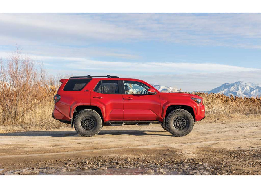 ReadyLIFT SST Lift Kit installed on a Toyota 4Runner: A red lifted Toyota 4Runner parked side-on, on a dirt road with mountains behind