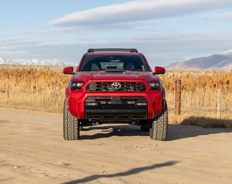 ReadyLIFT SST Lift Kit installed on a Toyota 4Runner: A red lifted Toyota 4Runner seen head-on, on a dirt road with dry reeds behind