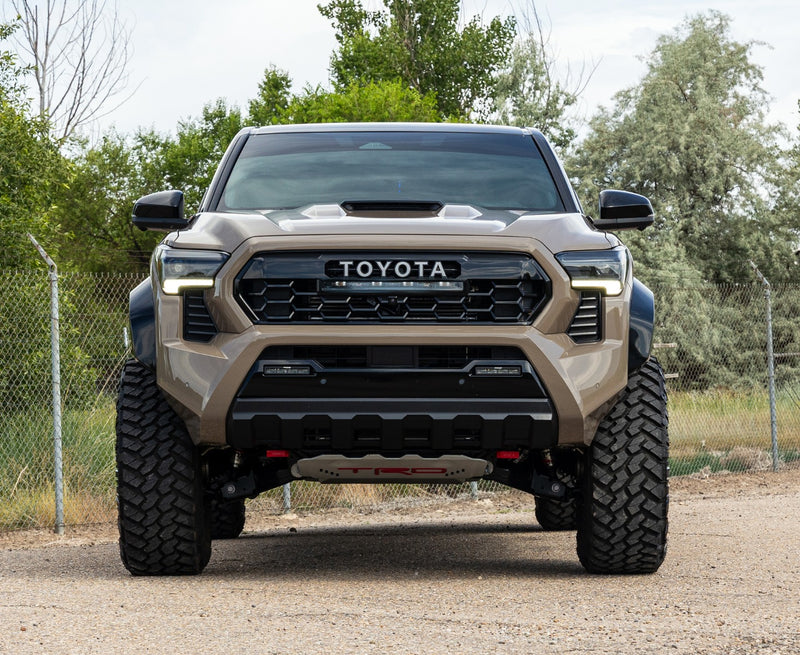 ReadyLIFT SST Lift Kit installed on a Toyota Tacoma: A tan lifted Toyota Tacoma TRD Pro seen head-on, on a gravel lot