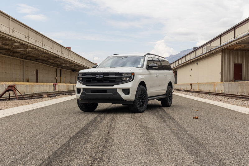 ReadyLIFT SST Lift Kit installed on a Ford Expedition: A white lifted Ford Expedition parked head-on between two long loading docks