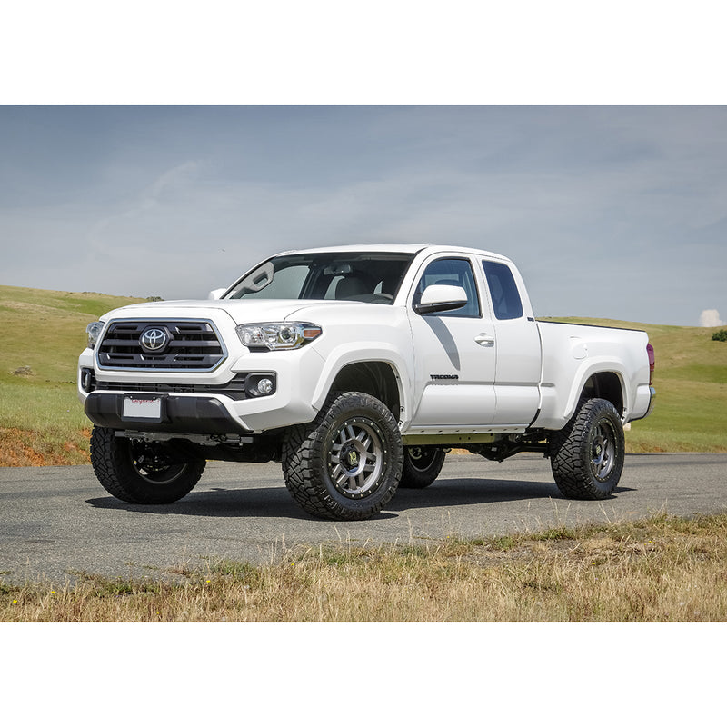 ReadyLIFT SST Lift Kit installed on a Toyota Tacoma: A white lifted Toyota Tacoma Access Cab on gray wheels parked on a road beside grass