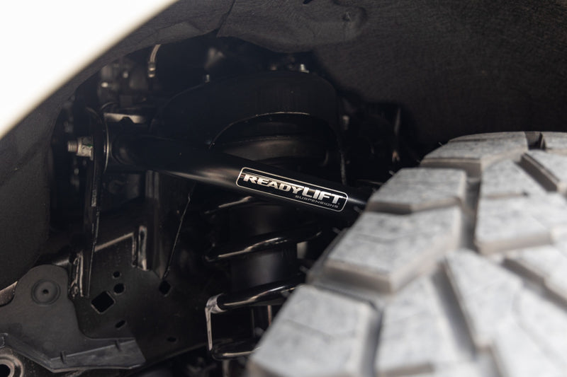 ReadyLIFT SST Lift Kit on a vehicle: close-up of a black ReadyLIFT upper control arm installed above an off-road tire in a wheel well
