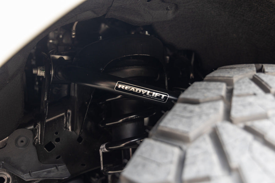 ReadyLIFT SST Lift Kit on a vehicle: close-up of a black ReadyLIFT upper control arm installed above an off-road tire in a wheel well