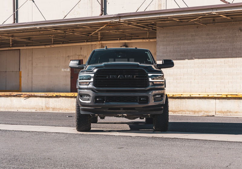 ReadyLIFT SST2.1 Coil Spring Lift Kit installed on a Ram 2500: A dark gray lifted Ram 2500 seen head-on in front of a loading dock