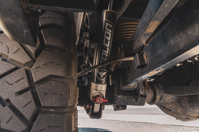 ReadyLIFT SST2.1 Coil Spring Lift Kit on a vehicle: underbody close-up of an installed Falcon shock with a red adjuster beside the axle and tire