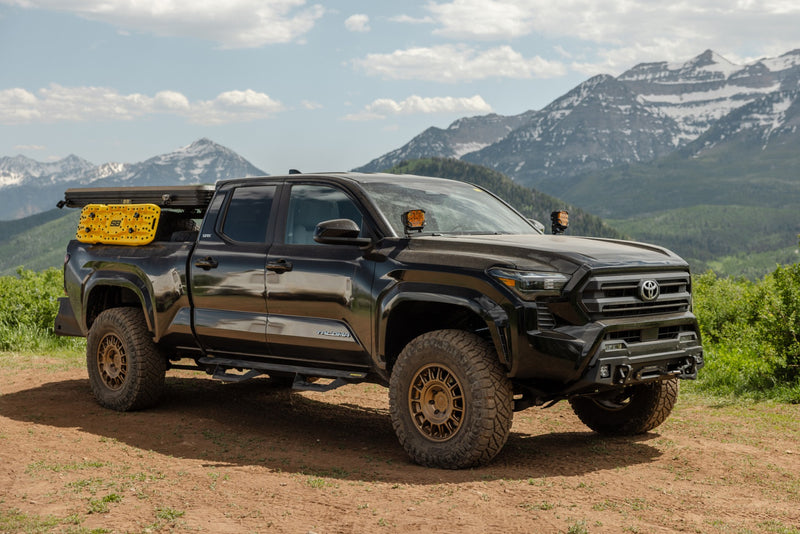 ReadyLIFT SST2.1 Suspension System installed on a Toyota Tacoma: A black lifted Toyota Tacoma with a bed rack parked on dirt with mountains behind