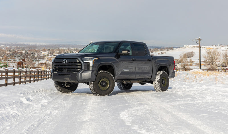 ReadyLIFT SST2.1 Suspension System installed on a Toyota Tundra: A gray lifted Toyota Tundra CrewMax parked on a snowy lot beside a fence