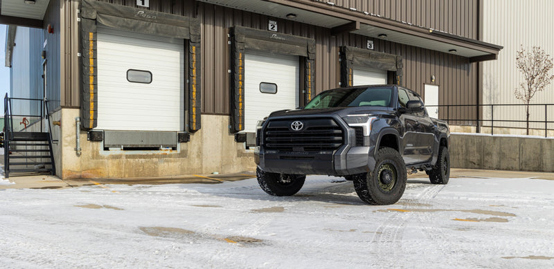 ReadyLIFT SST2.1 Suspension System installed on a Toyota Tundra: A gray lifted Toyota Tundra CrewMax parked on snow in front of warehouse loading doors