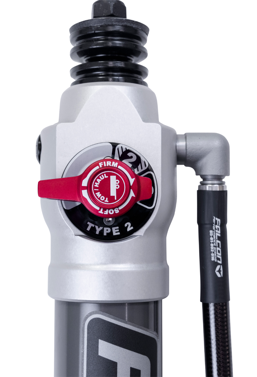 Close-up of the ReadyLIFT SST2.1 Suspension System: close-up of a silver Falcon shock body with a red Type 2 firm-soft adjuster knob on a black background