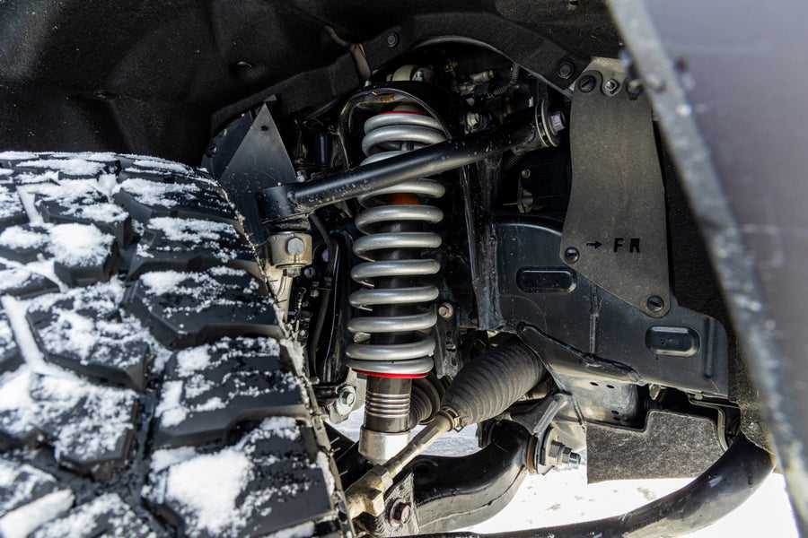 ReadyLIFT SST2.1 Suspension System on a vehicle: close-up of an installed Falcon coilover and upper control arm behind a snow-covered tire