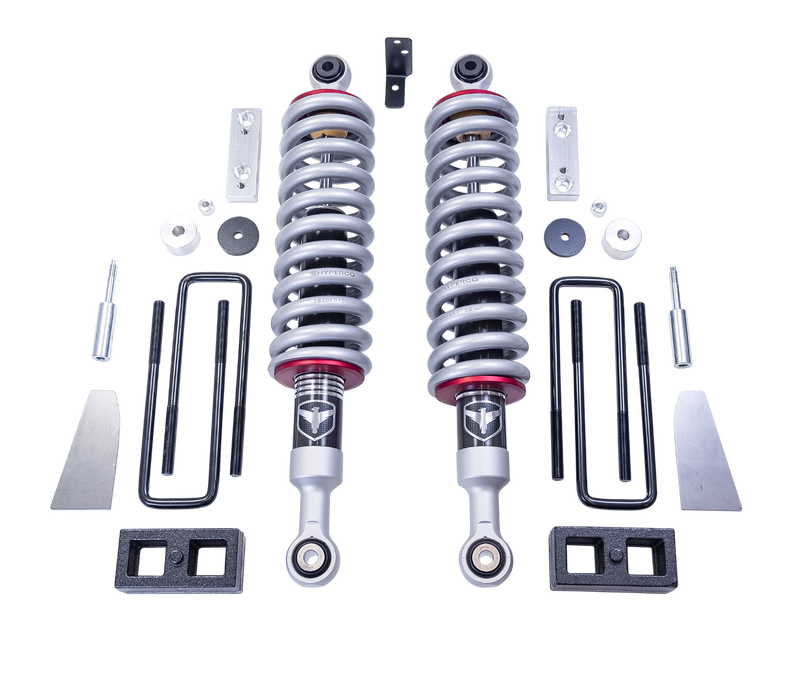 ReadyLIFT SST2.1 Suspension System, full kit on a studio background: two Falcon coilovers with silver springs, rear blocks, U-bolts, aluminum brackets and spacers on a black background