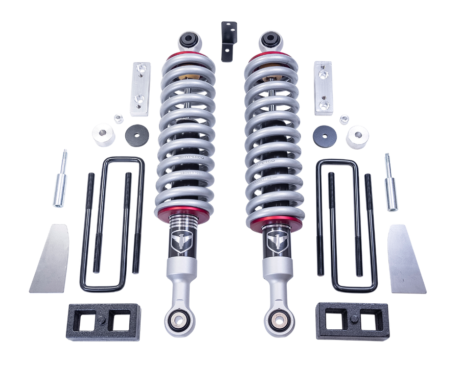 ReadyLIFT SST2.1 Suspension System, full kit on a studio background: two Falcon coilovers with silver springs, rear blocks, U-bolts, aluminum brackets and spacers on a black background