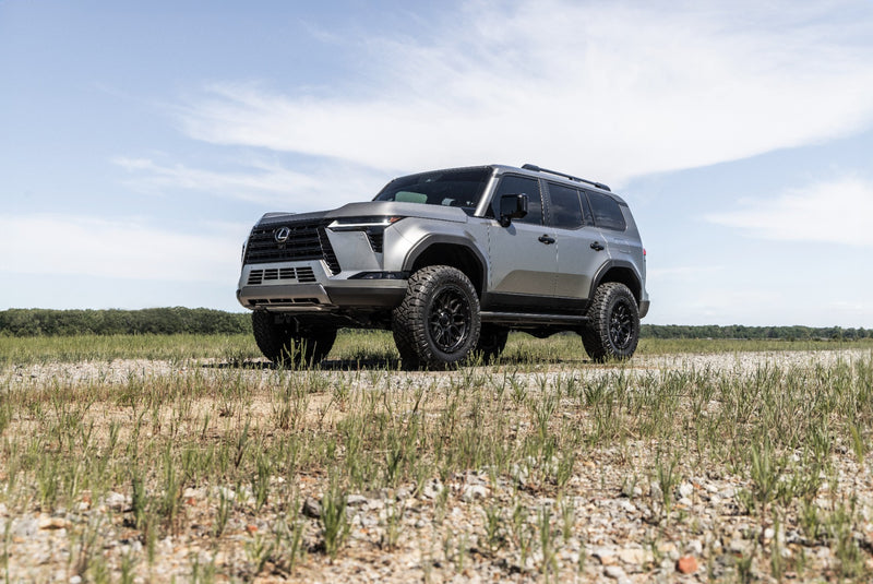 ReadyLIFT SST3.3 Suspension System installed on a Lexus GX550: A silver lifted Lexus GX550 parked on a gravel track in a grass field, lower angle