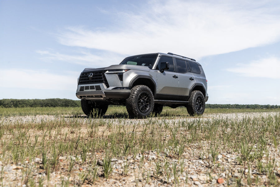 ReadyLIFT SST3.3 Suspension System installed on a Lexus GX550: A silver lifted Lexus GX550 parked on a gravel track in a grass field, lower angle