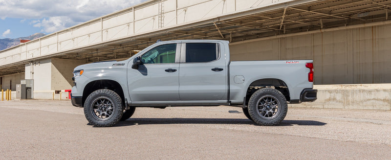 ReadyLIFT Suspension System installed on a Chevrolet Silverado 1500: A gray lifted Chevrolet Silverado 1500 Crew Cab parked side-on by a loading dock