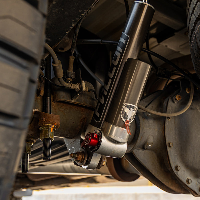ReadyLIFT Suspension System on a vehicle: Falcon reservoir shock with red adjuster installed beside the leaf spring and axle under a truck