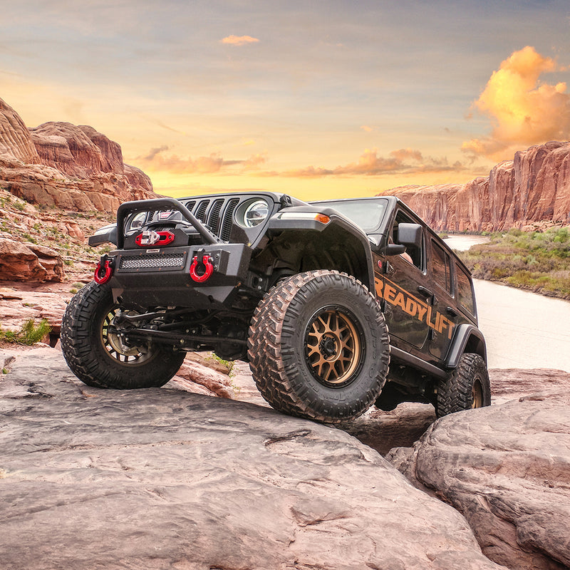 ReadyLIFT Terrain Flex 4-Arm Kit installed on a Jeep Wrangler JL: A black lifted Jeep Wrangler with ReadyLIFT graphics flexing over slickrock with red cliffs at sunset
