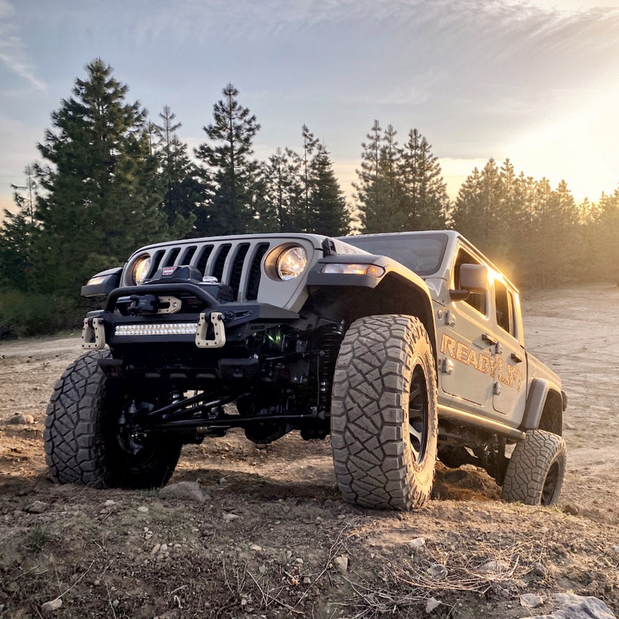 ReadyLIFT Terrain Flex 4-Arm Lift Kit installed on a Jeep Gladiator: A gray lifted Jeep Gladiator with a ReadyLIFT decal on a dirt trail with pine trees at sunset