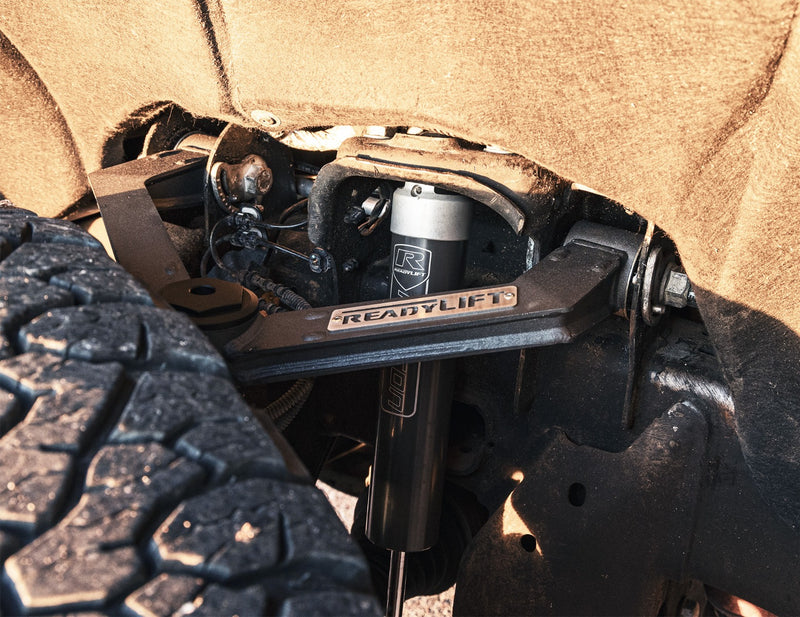 ReadyLIFT Xtreme-Duty Fabricated A-Arm Kit on a vehicle: A black fabricated ReadyLIFT upper control arm installed above a tire next to a black coilover shock