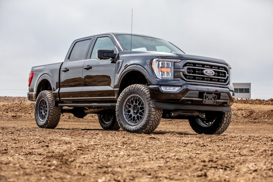 Big Lift Kits by ReadyLIFT: Black Ford F-150 crew cab lifted on mud-terrain tires on a dirt lot, front quarter view.
