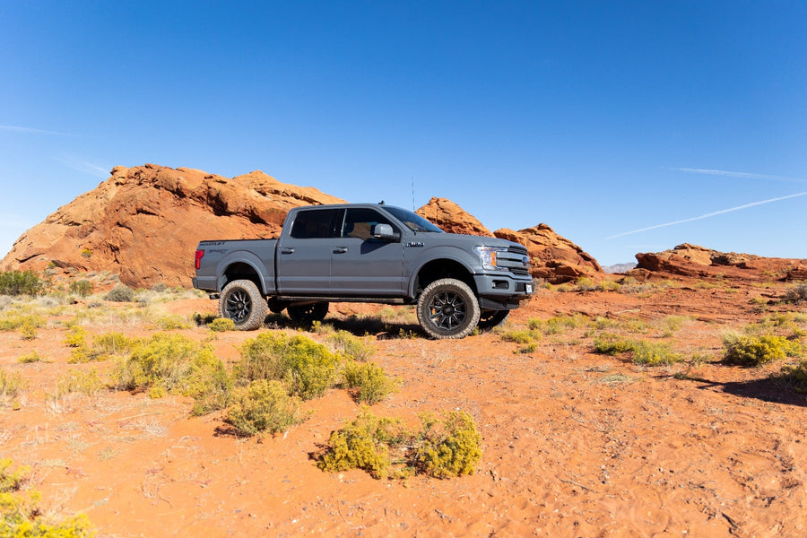Big Lift Kits by ReadyLIFT: Gray Ford F-150 crew cab lifted on black wheels among red rock formations in the desert, wide view.