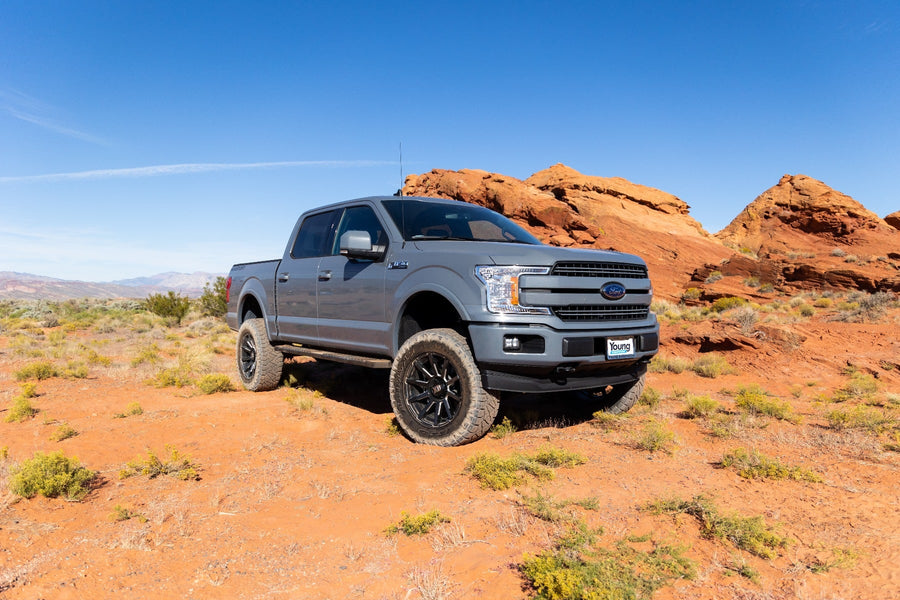 Big Lift Kits by ReadyLIFT: Gray Ford F-150 crew cab lifted on black wheels in red desert terrain under blue sky.