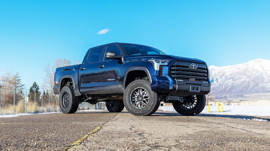 Big Lift Kits by ReadyLIFT: Dark blue Toyota Tundra crew cab lifted on black wheels on a cracked road with snowy mountains behind.