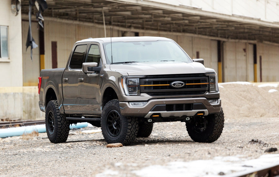 Leveling Kits by ReadyLIFT: Gray Ford F-150 Tremor crew cab lifted on black wheels on gravel in front of a warehouse.