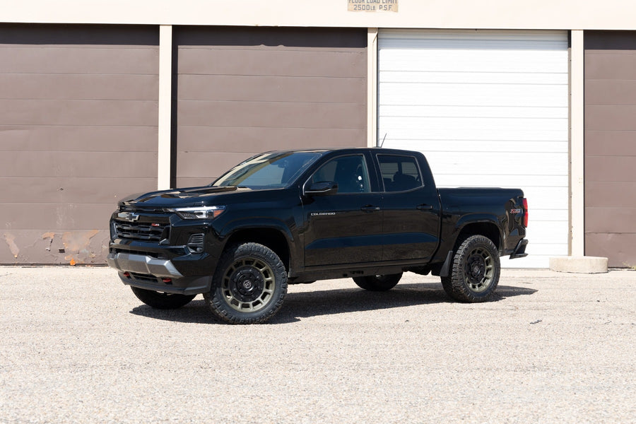 Leveling Kits by ReadyLIFT: Black Chevrolet Colorado crew cab leveled on bronze wheels in front of storage doors.