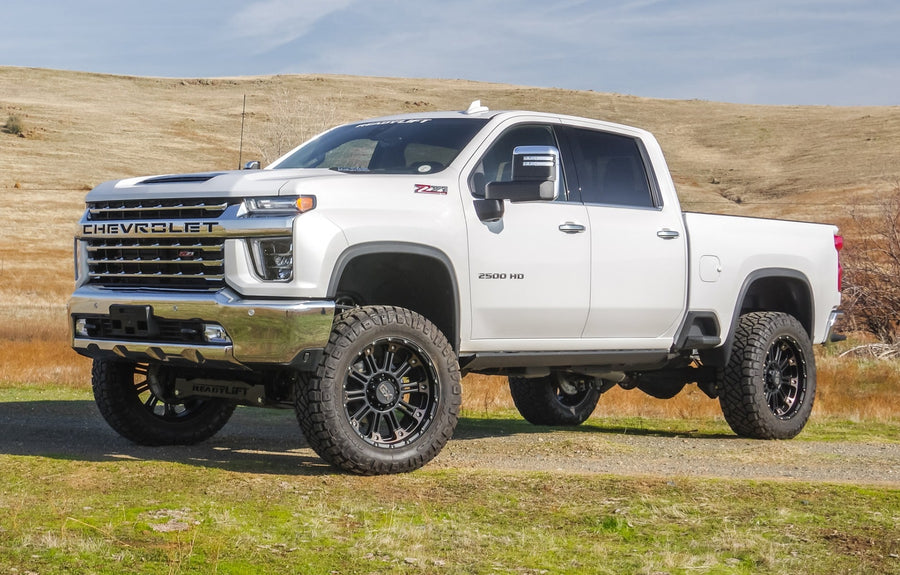 MAX Suspension Systems by ReadyLIFT: White Chevrolet Silverado 2500HD crew cab lifted on black wheels in a grassy field.