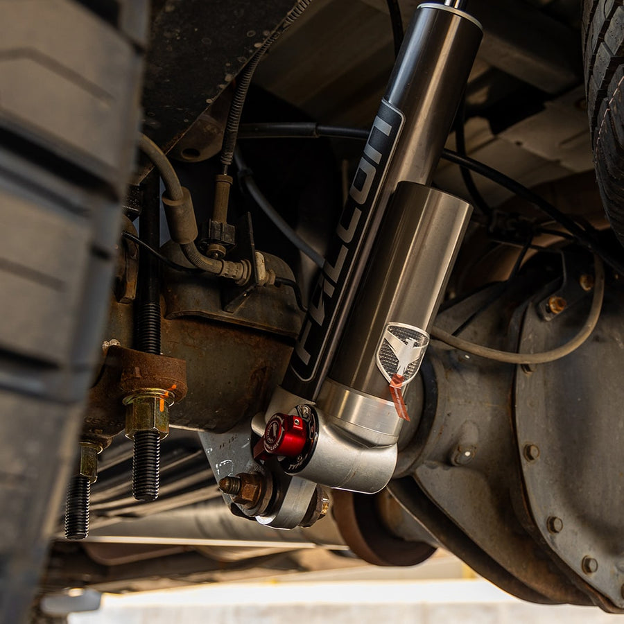 MAX Suspension Systems by ReadyLIFT: Falcon reservoir shock with red adjuster installed beside the leaf spring and axle under a truck.