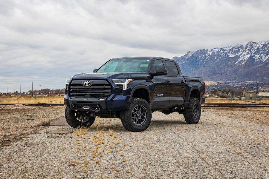 MAX Suspension Systems by ReadyLIFT: Dark blue Toyota Tundra crew cab lifted with an aftermarket bumper on a gravel lot below snowy mountains.