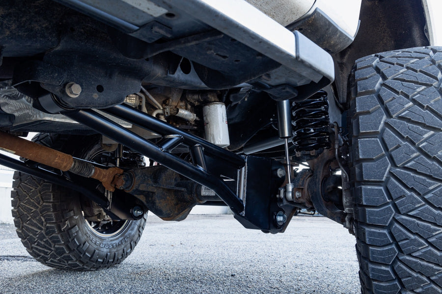 Radius Arms by ReadyLIFT: Black tubular radius arm installed under a Super Duty front axle beside a large tire.