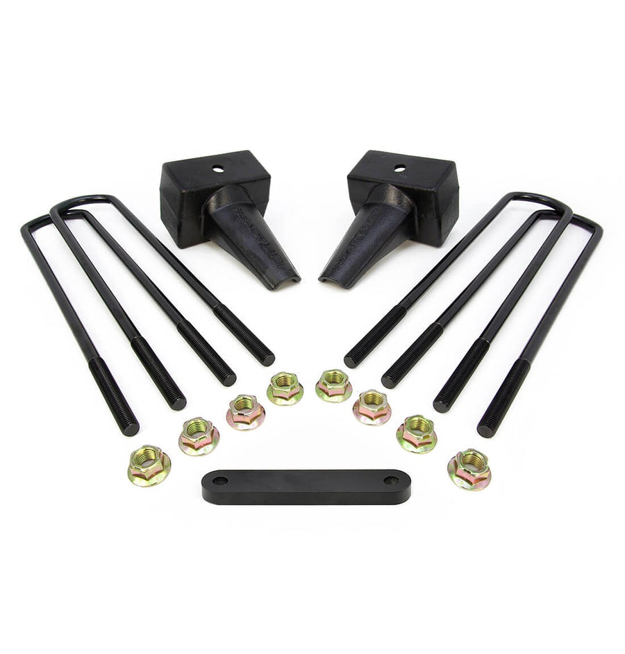 Rear Block Kits by ReadyLIFT: Two black tapered 4" rear lift blocks with four square U-bolts, gold nuts and a spacer plate on white.