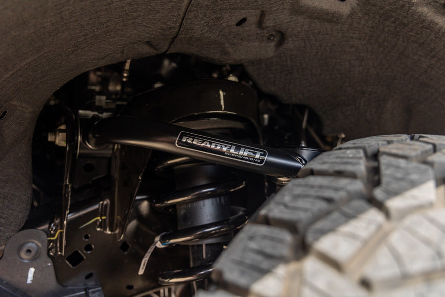 SST Lift Kits by ReadyLIFT: Close-up of a black ReadyLIFT upper control arm installed behind an off-road tire in a wheel well.