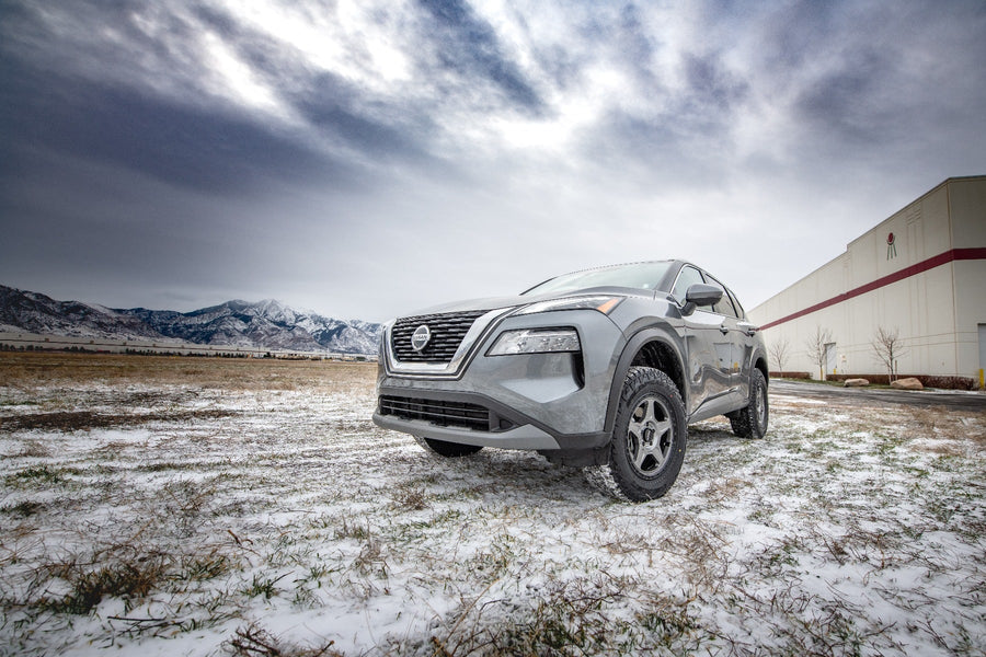 SST Lift Kits by ReadyLIFT: A gray lifted Nissan Rogue on a snowy lot beside a building under cloudy sky.
