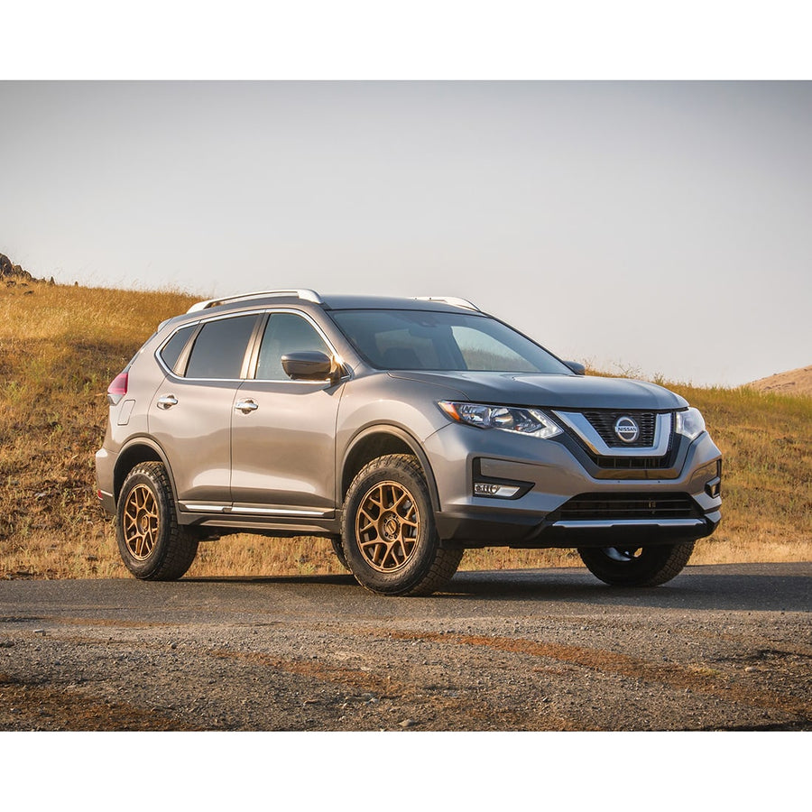 SST Lift Kits by ReadyLIFT: A gray lifted Nissan Rogue on bronze wheels parked on a dirt road in a dry field.