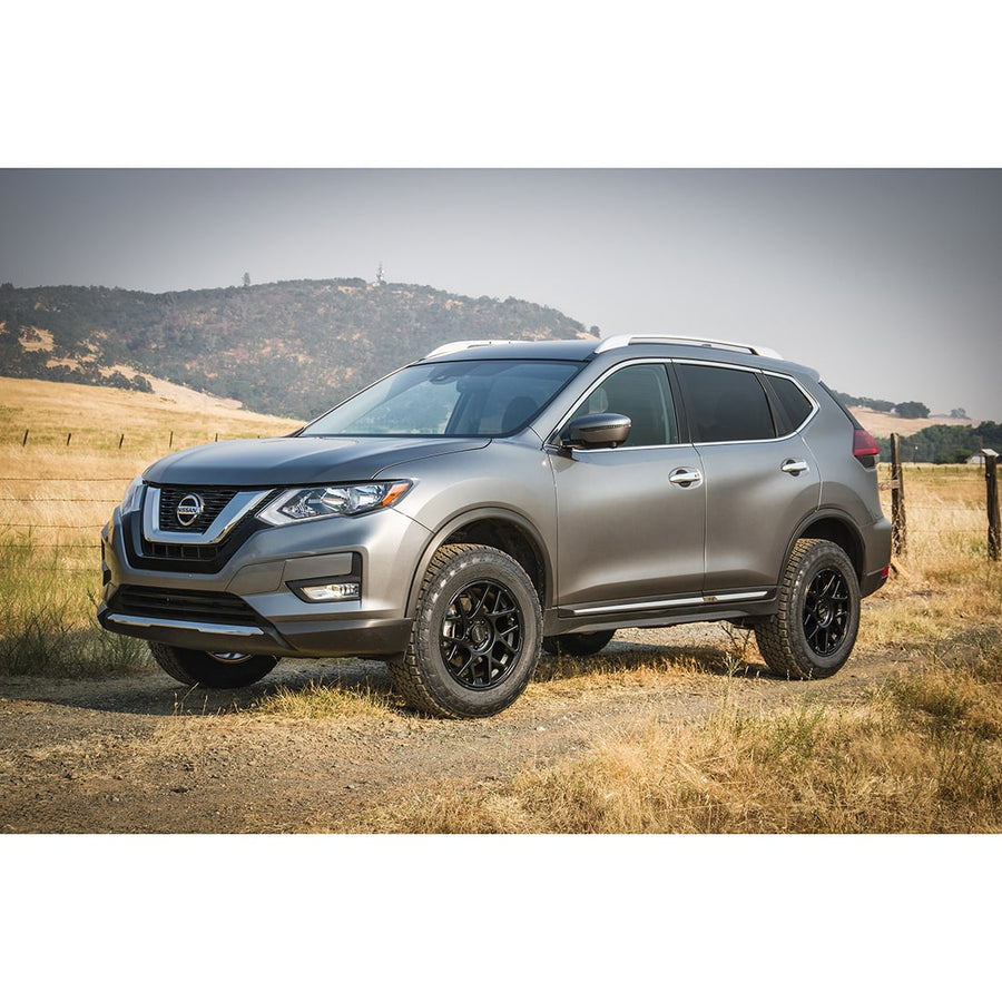 SST Lift Kits by ReadyLIFT: A gray lifted Nissan Rogue on black wheels parked on dirt beside a fenced field.